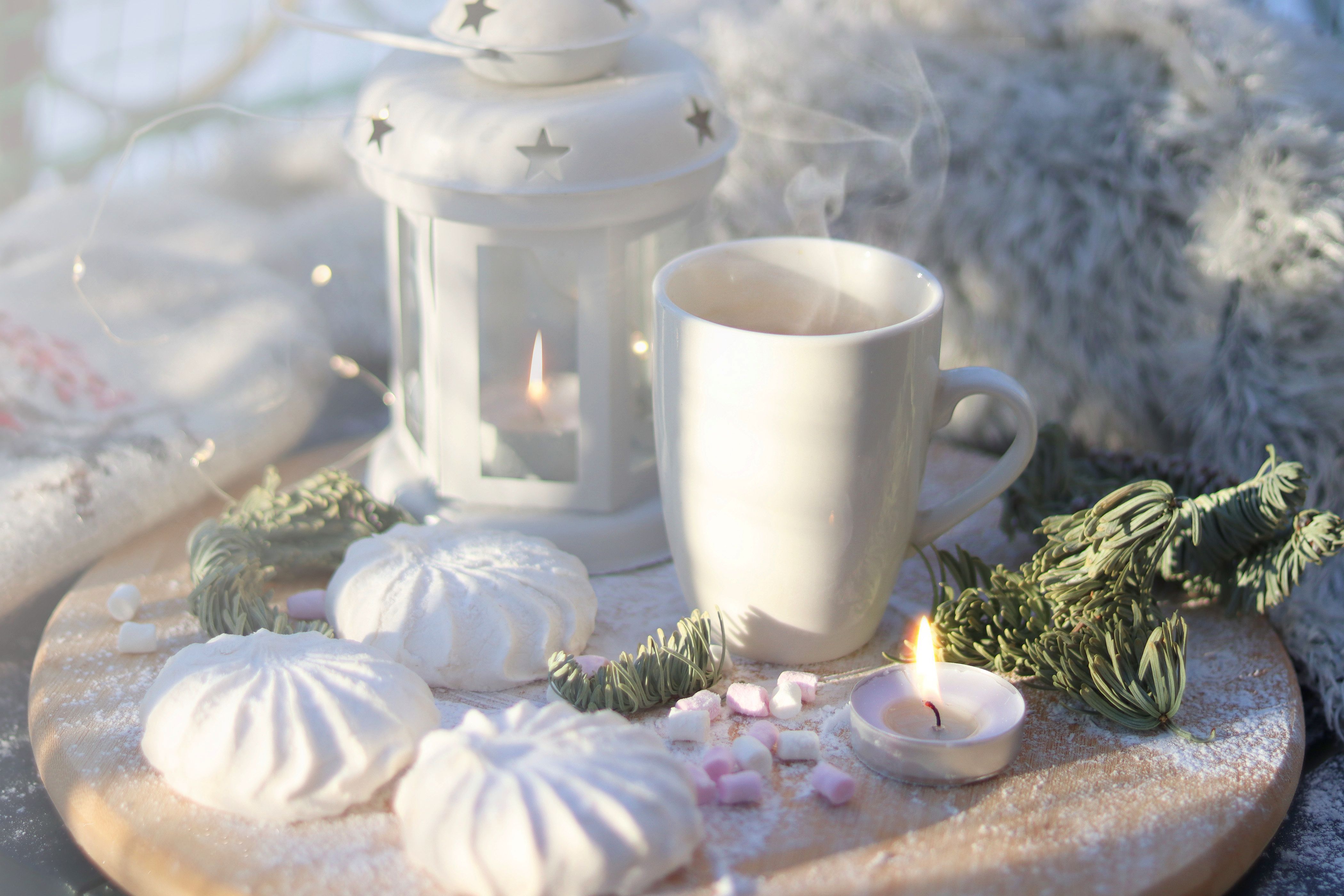 White lantern with a candle beside a steaming mug, tea lights and pine sprigs for a restful winter evening