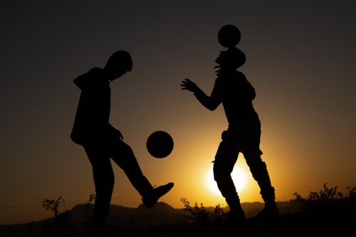 Free Silhouetted soccer players performing tricks at sunset, creating a scenic and dramatic view. Stock Photo