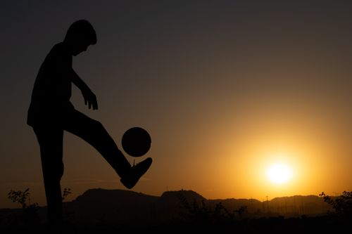 Free A person silhouetted against a sunset, juggling a soccer ball in a serene outdoor setting. Stock Photo