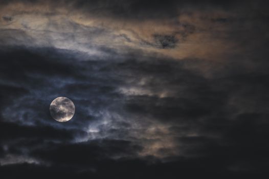 夜空中，黑暗而喜怒无常的满月被引人注目的云层环绕
