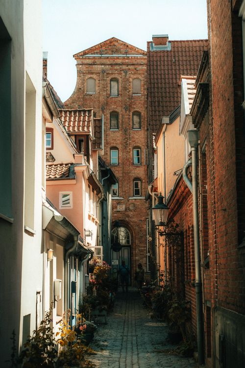 Free A narrow cobblestone alleyway lined with historic brick buildings and vintage lamps. Stock Photo