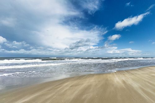 Free A serene beach scene with rolling waves under a blue sky at Borkum, Germany. Stock Photo