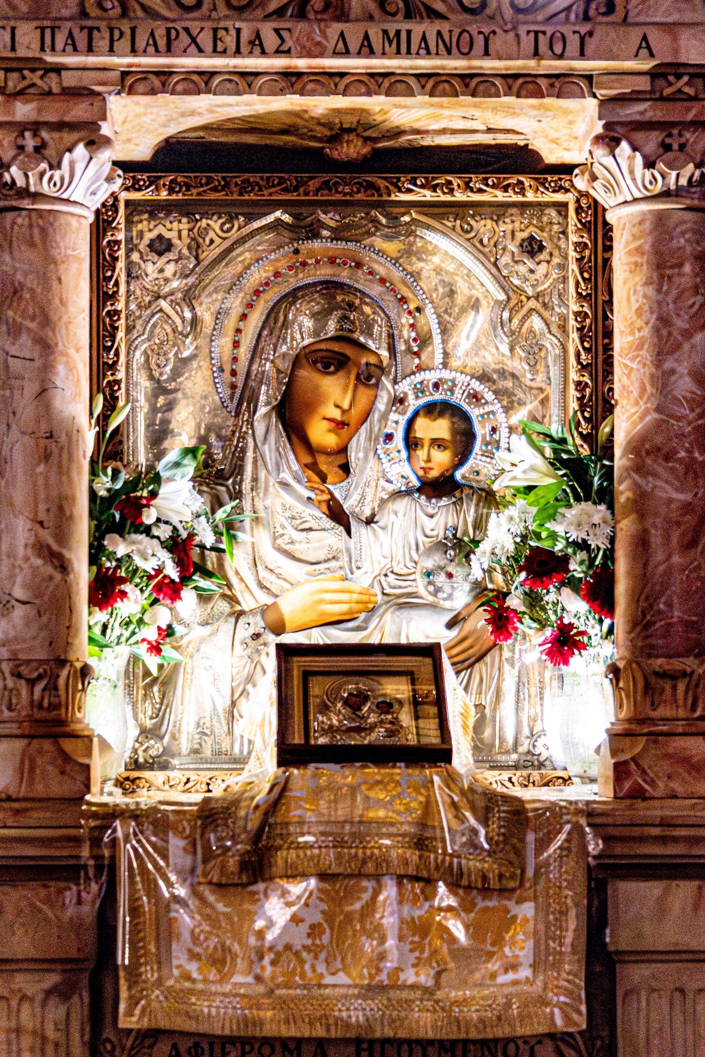 Iconostasis featuring Virgin Mary and Child, adorned with floral arrangements in Jerusalem church.