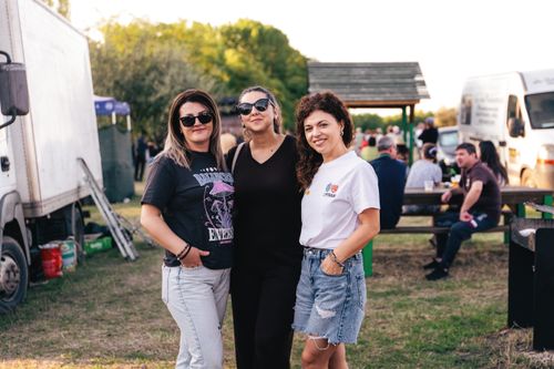 Free Three friends enjoying an outdoor event at sunset with people in the background. Stock Photo