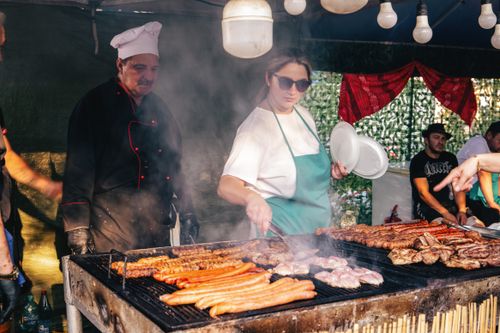Free Chefs grill sausages and meats at an outdoor BBQ stall, creating delicious street food. Stock Photo