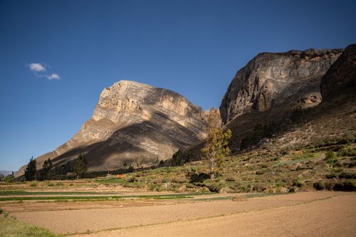 Free A breathtaking view of mountains under a clear blue sky with fields in the foreground, offering a serene natural landscape. Stock Photo