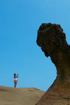 A woman captures a photo of a distinctive rock formation under a clear blue sky.