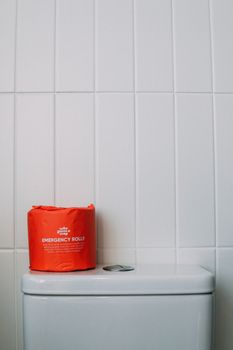 Red emergency toilet paper roll on a white toilet in a minimalist bathroom setting.