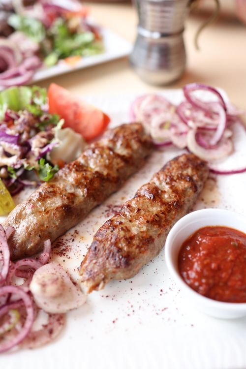 Free Appetizing grilled kebabs with fresh salad, onions, and spicy tomato sauce on a plate. Stock Photo