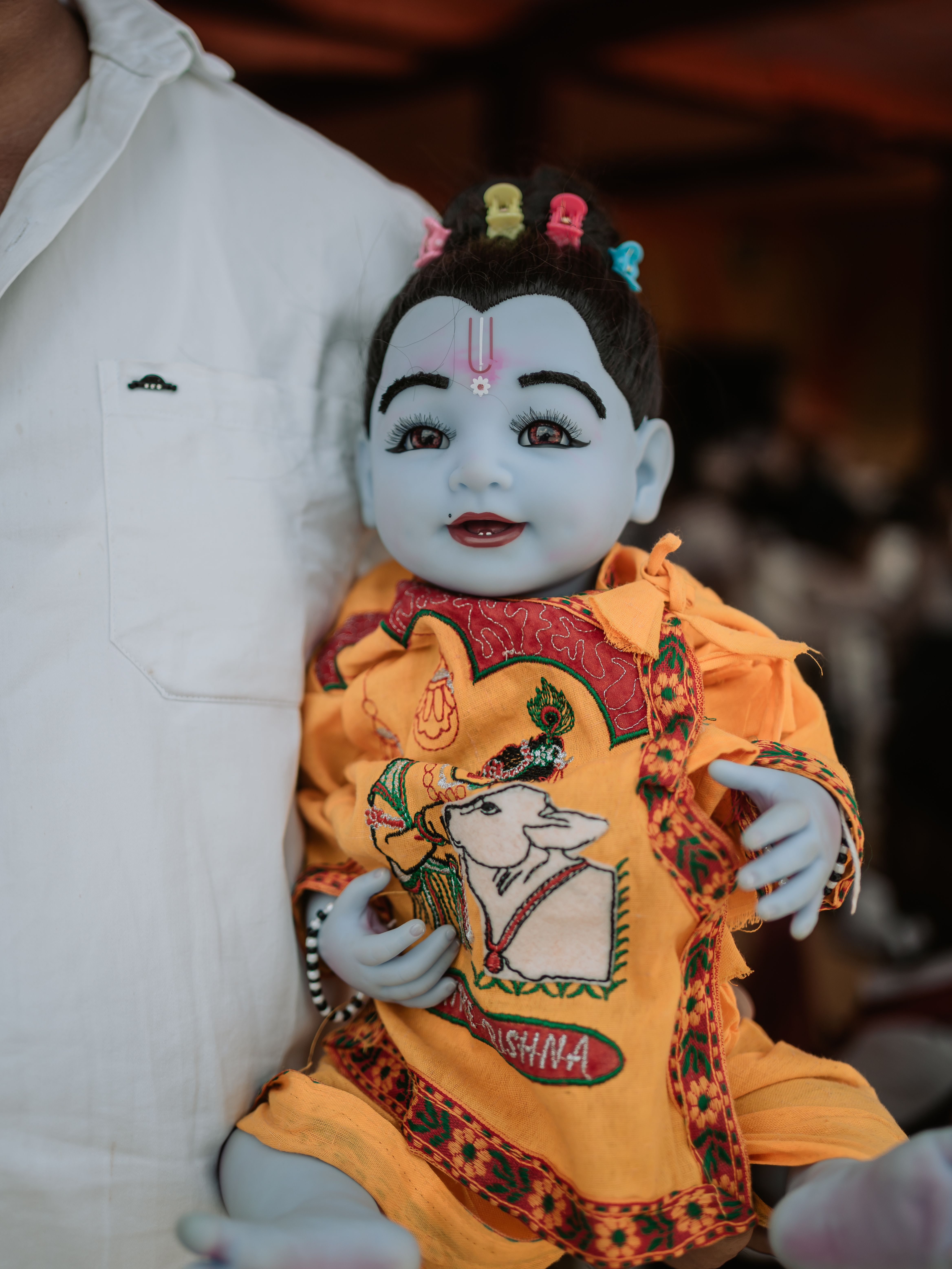 Close-up of a Krishna doll dressed in colorful traditional attire held by an adult.