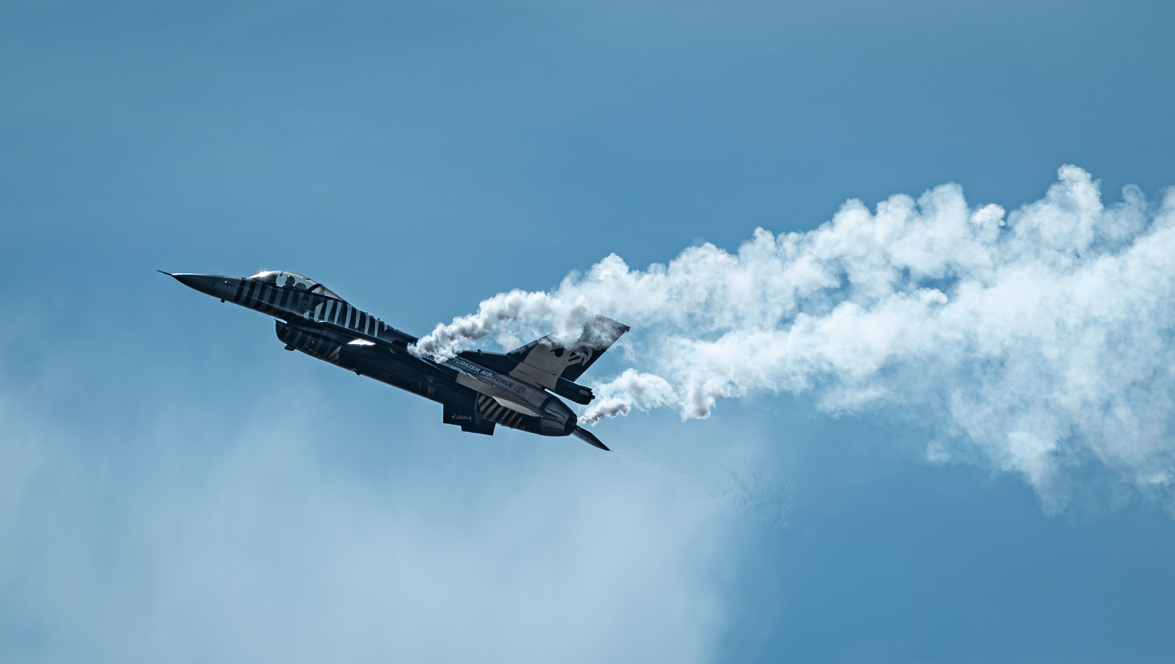 Stunning image of a fighter jet executing aerial acrobatics with smoke trails against a clear blue sky.