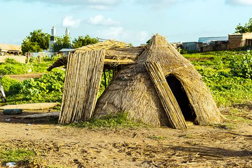 Free A traditional straw hut surrounded by greenery in a rural setting under a bright sky. Stock Photo