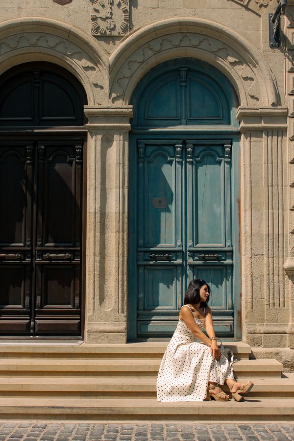 A woman in a white dress sits on the steps of a historic building in Baku, Azerbaijan.