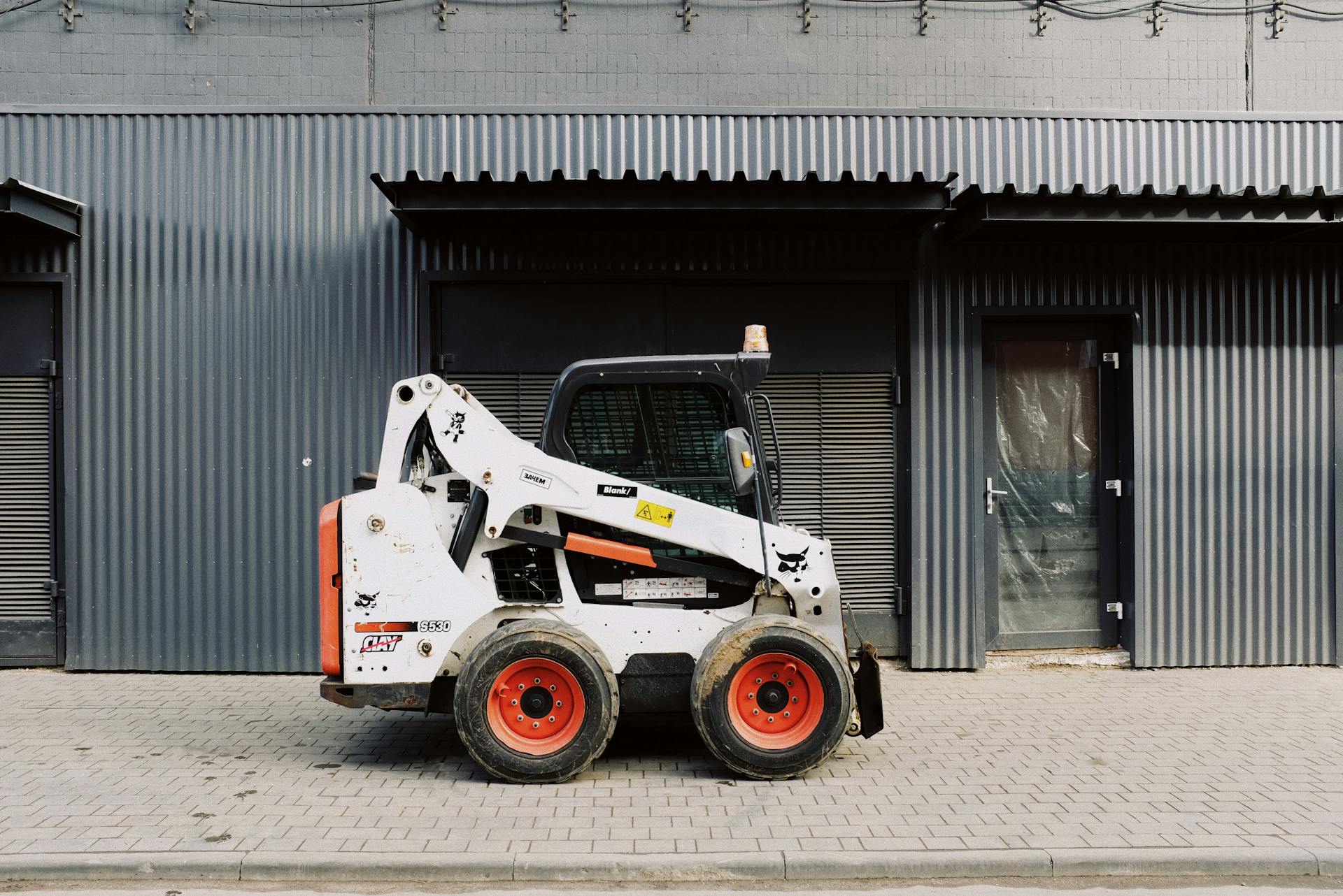 Small white truck loader parked on pavement near black wall of modern building on street in city