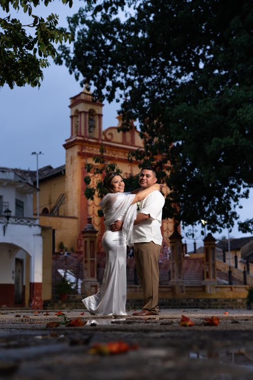 Free Couple in elegant attire stands lovingly before historic church in Comitán, Mexico. Stock Photo