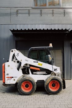 A modern skid steer loader parked outside a building for industrial work.