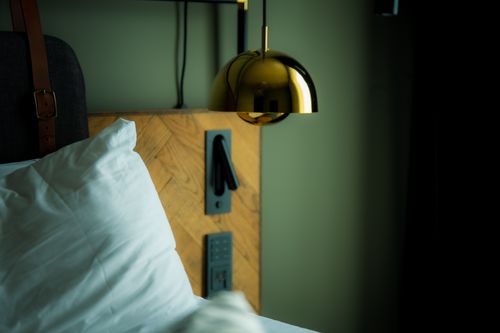 Free A comfortable bedroom setup featuring a soft pillow and elegant gold lamp for a modern vibe. Stock Photo