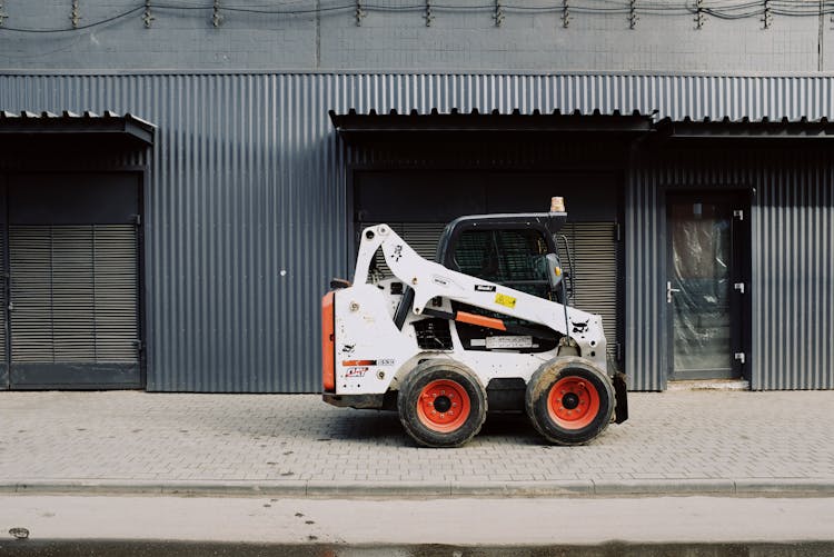 Small Truck Parked Near Warehouse On Sidewalk On Street