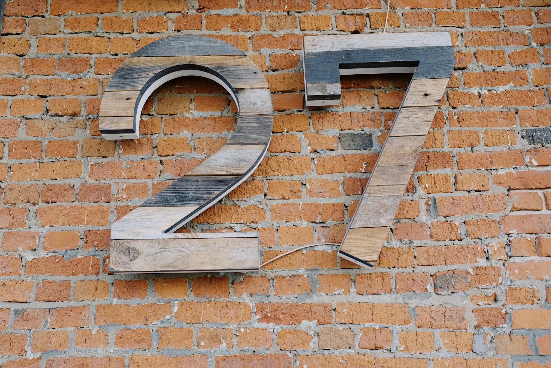Big wooden number sign hanging on brick wall of modern building