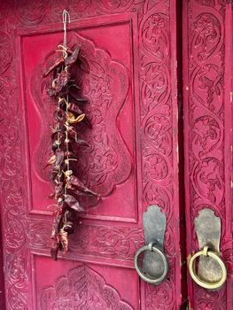 Detailed red door in Tashkent with hanging dried peppers, showcasing intricate carvings.