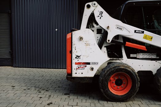 Close-up of a modern skid steer loader parked outdoors on a paved surface.