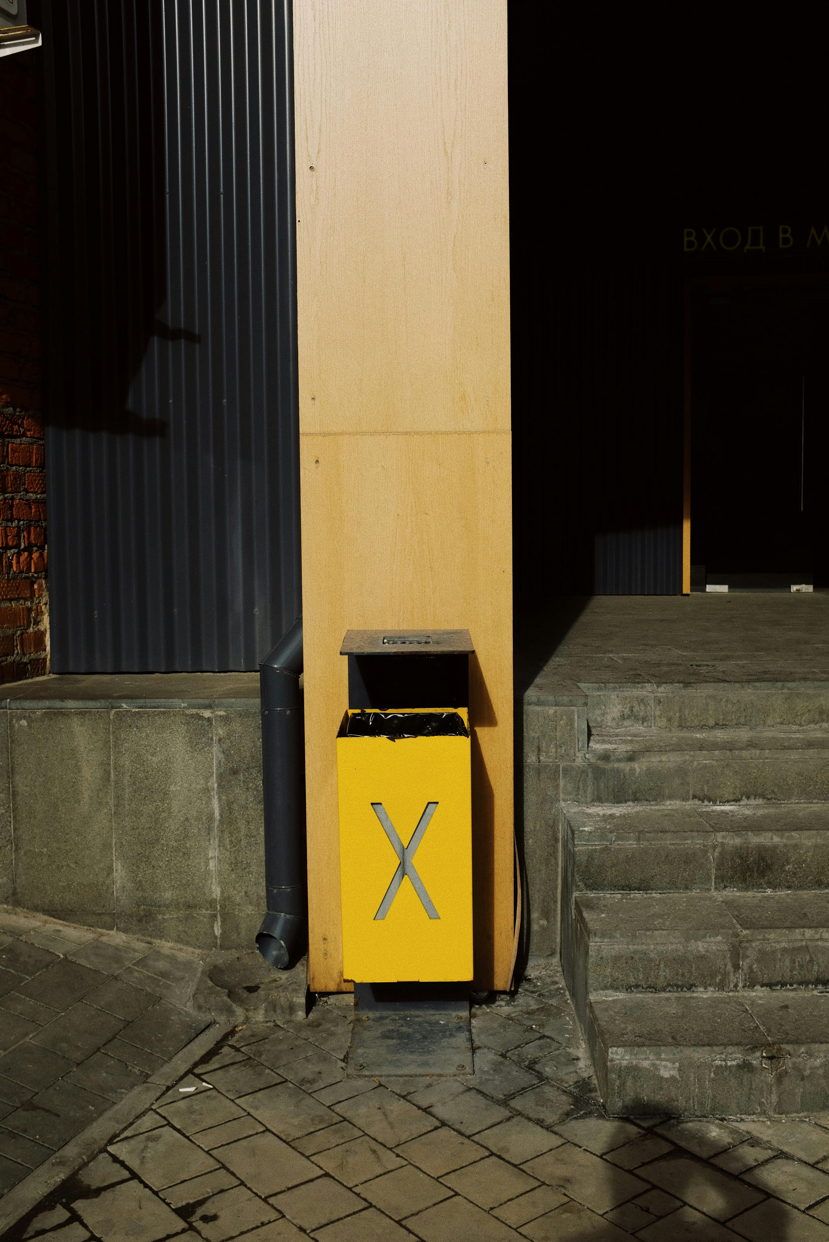 Yellow metal trash box placed near column of modern building on street in city