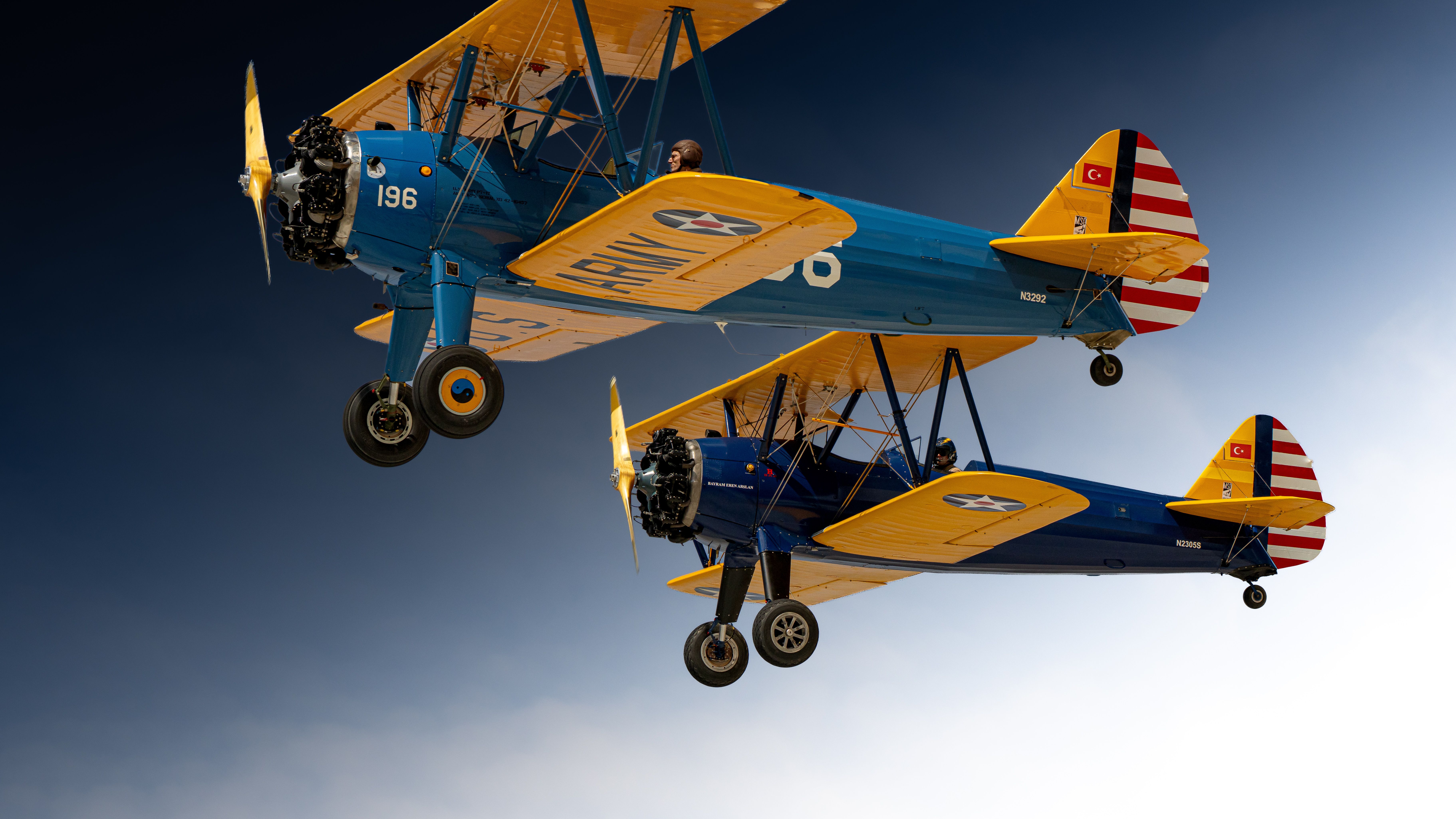 Two vintage biplanes flying side by side against a clear blue sky.