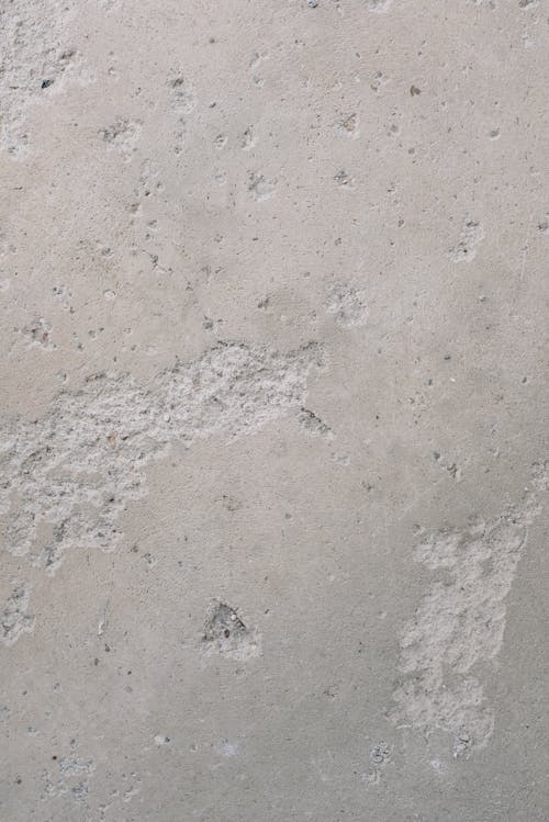 Aged rough concrete wall covered with small cracks and stains on street in city