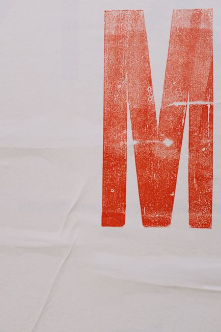 White paper poster with printed colorful letter M placed on wall on street