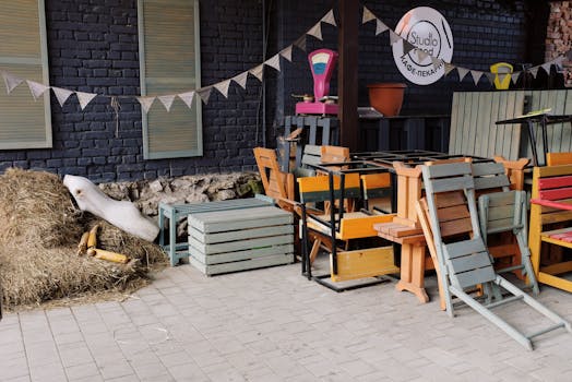 Street paved yard of small cafe with folded wooden chairs and benches placed on each other and body of mannequin on haystack near brick wall