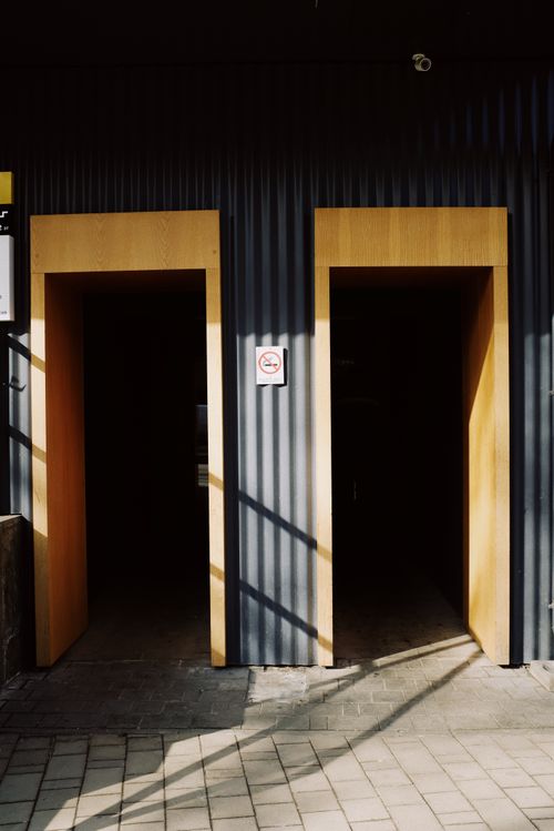 Free Opposite wooden doorways in black metal wall with sign prohibiting to smoke on sunny street in city Stock Photo