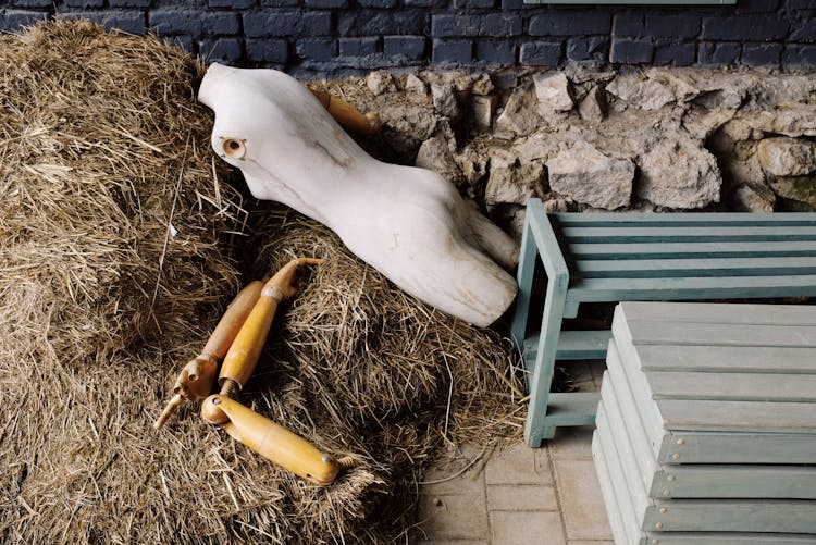 Body Of Mannequin Placed On Haystacks Near Black Brick Wall