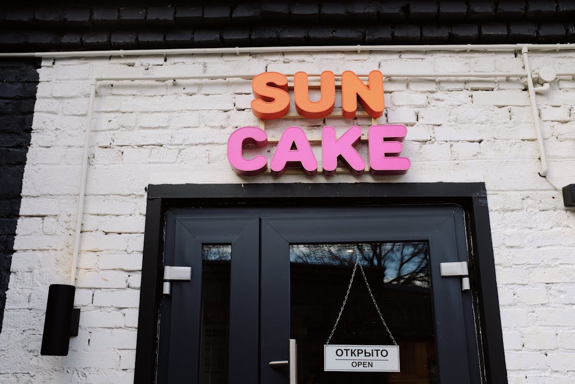 Exterior of modern cafe with glass door and bright signboard on white brick wall