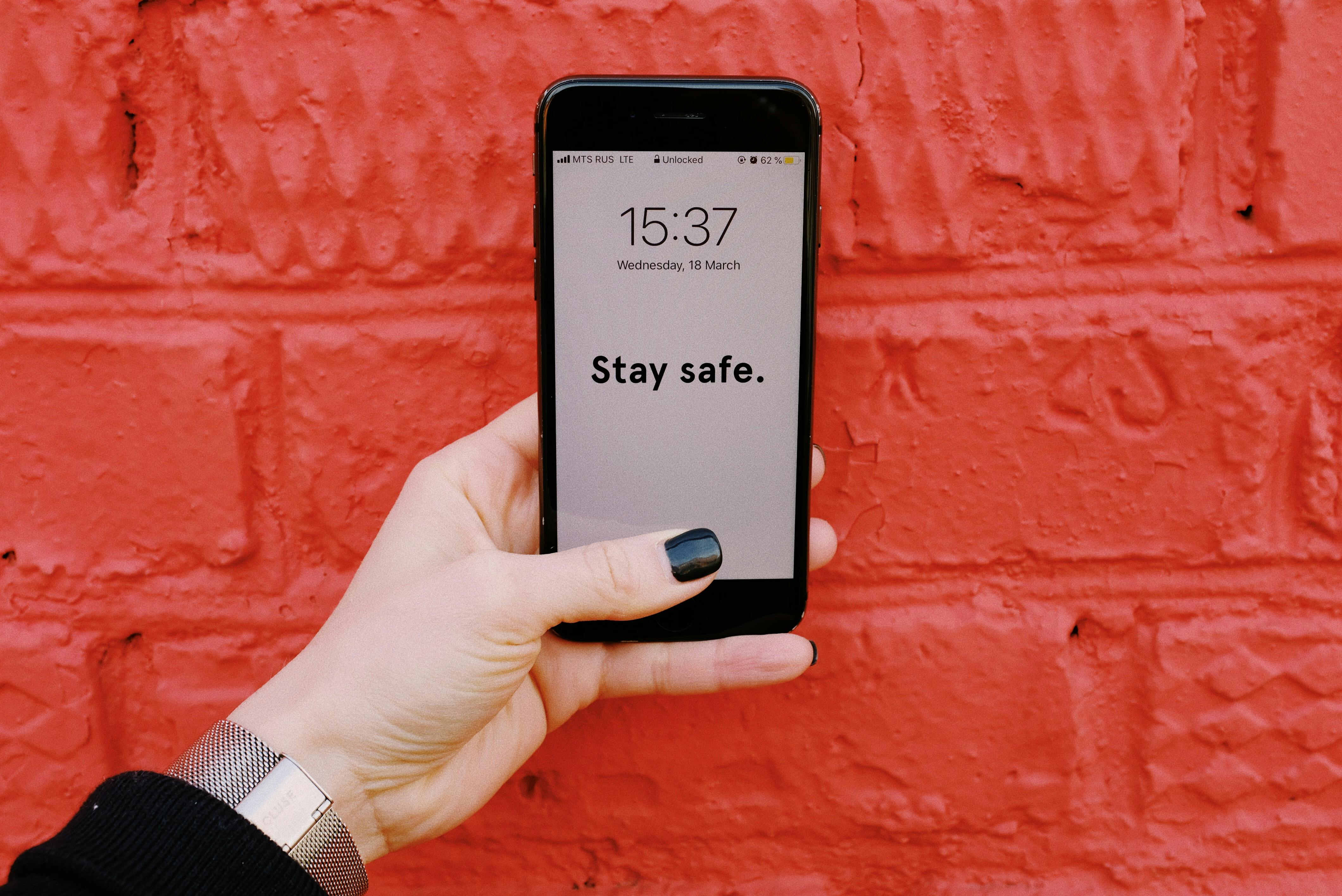 Anonymous crop woman demonstrating smartphone with inscription Stay sage on screen near brick wall painted red
