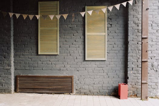 An outdoor scene featuring a minimalist brick wall with shutters and a garland, highlighting urban design.