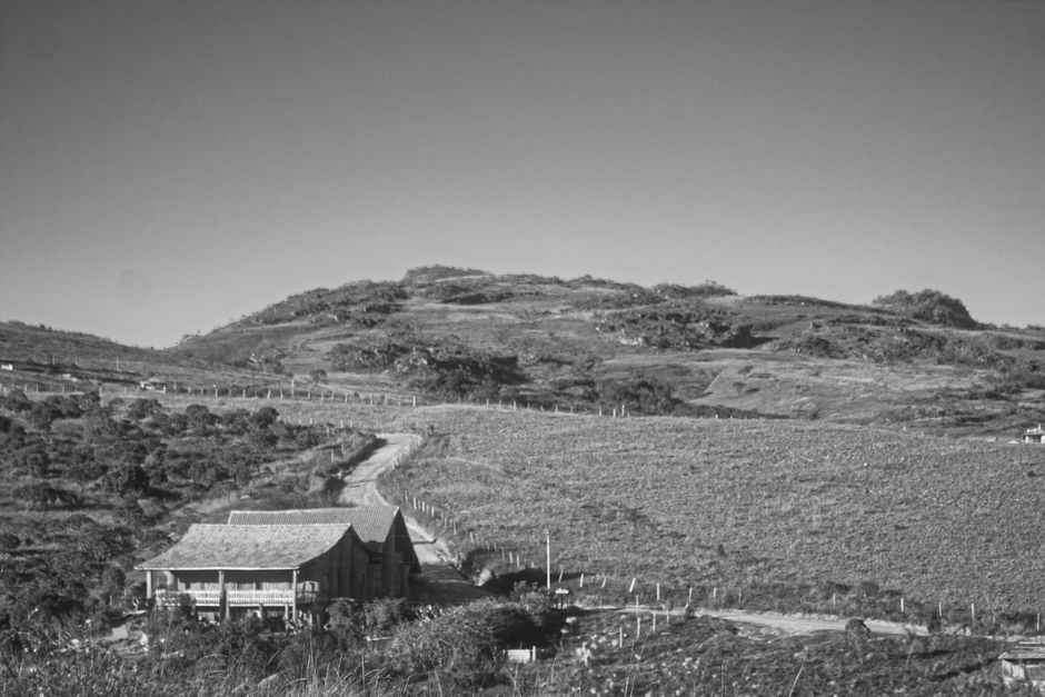 Black and white rural scene in São Thomé das Letras, displaying a farmhouse amidst rolling hills.