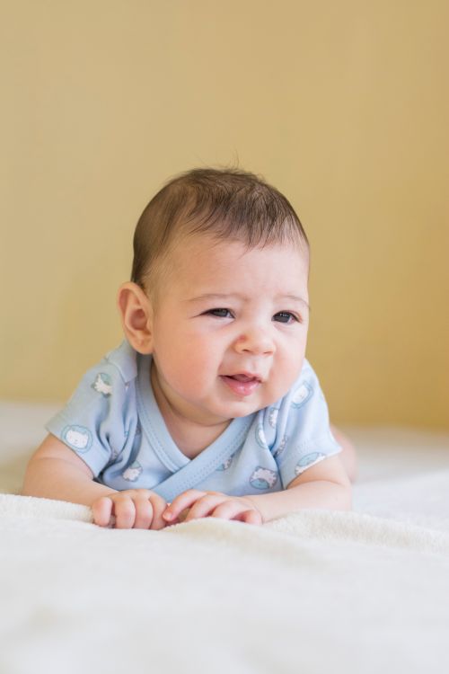 Free A cute baby lying on a bed wearing a blue onesie, expressing curiosity. Stock Photo