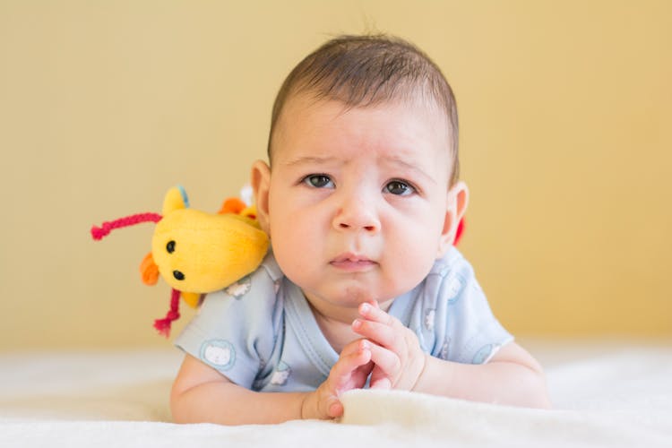 Baby In Blue Shirt Lying On Bed