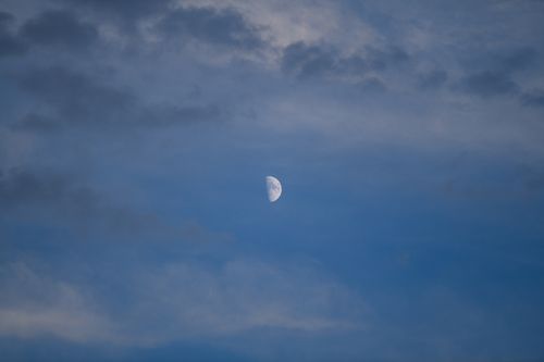 Free A serene view of the half moon surrounded by soft, cloudy blue skies. Stock Photo