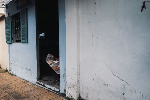 Free A serene street view showing a doorway in Sa Đéc, Việt Nam with a person reading a newspaper. Stock Photo