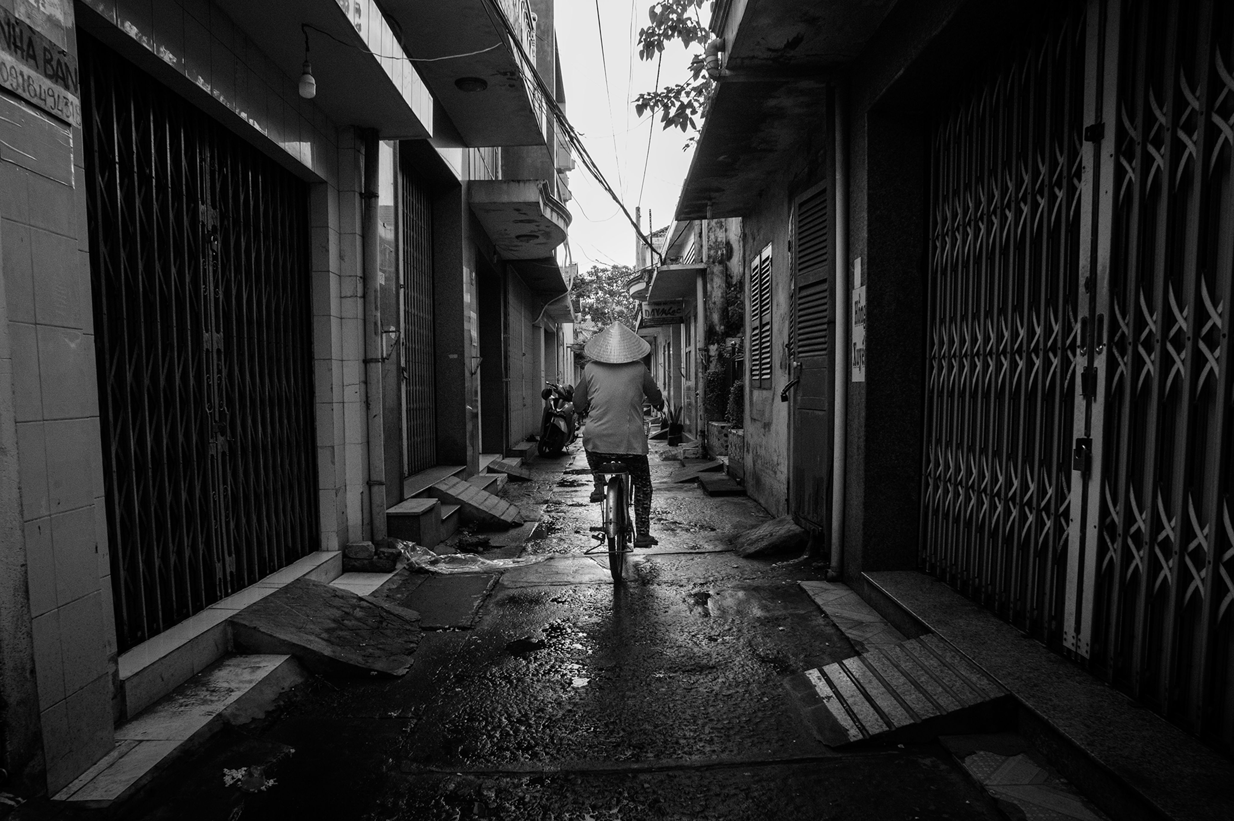 A person cycling in a narrow, wet alleyway in Sa Đéc, Vietnam, showcasing daily life.