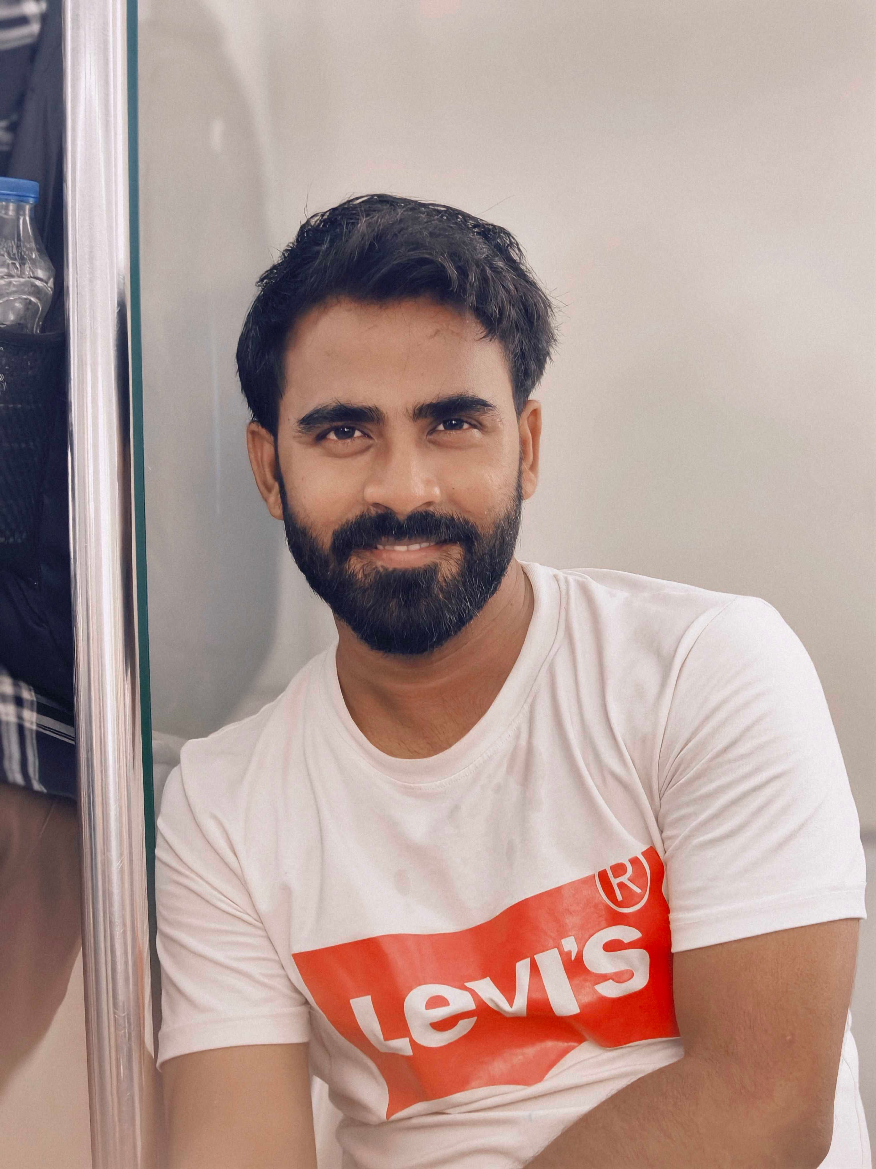 Portrait of a man in a Levi's t-shirt sitting indoors, smiling warmly.