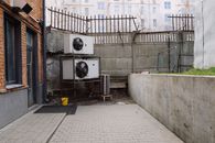 Air conditioning system located outside concrete shabby fence with metal barrier near industrial building from bricks and glass door