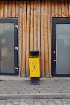 Yellow and black bin located between two glass doors in wooden wall on modern pavement in city