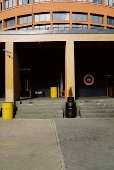 Contemporary urban building facade with colorful barrels and steps leading to entrances.