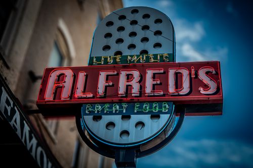 Free Vintage neon sign for Alfred's showcasing live music and great food outside an urban building. Stock Photo
