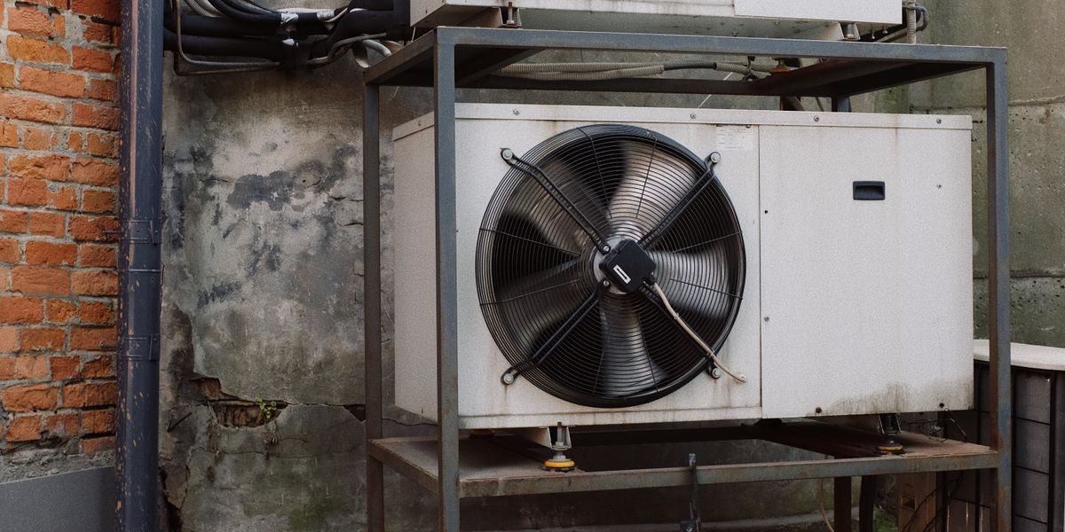 HVAC technician in uniform servicing a residential air conditioner condenser unit outside a home