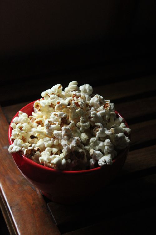 Free A dimly lit red bowl filled with popcorn on a wooden table, perfect for snack time. Stock Photo