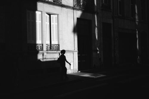Free Silhouette of a person walking on a shadowy city street during the day. Stock Photo