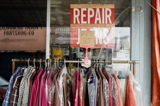 A clothing rack with various garments outside a tailor shop with a repair sign.